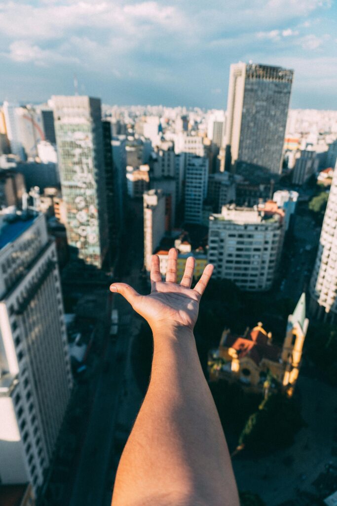 Hand reaching towards a vibrant city skyline on a clear day, capturing urban life.